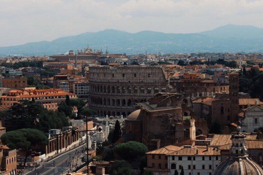 The Colosseum in Rome surrounded by historic buildings and mountains in the background. 5