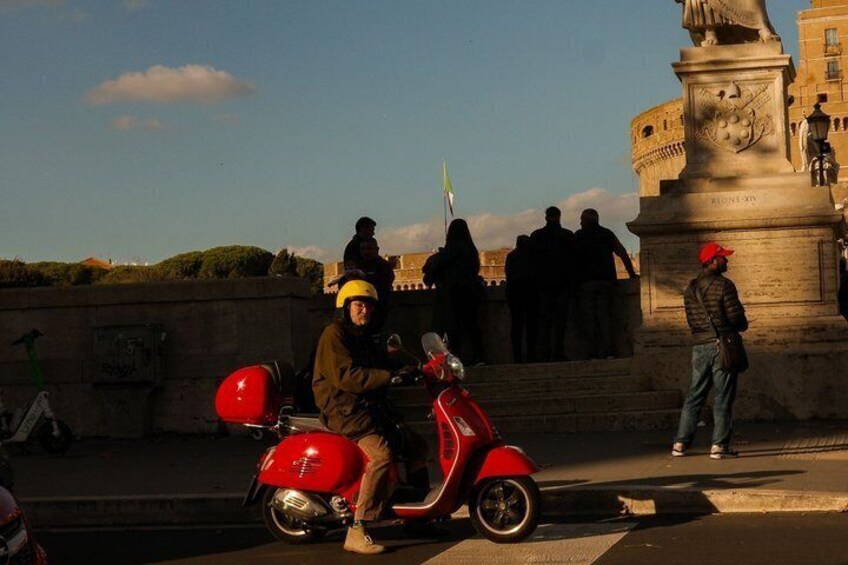 A person on a red scooter, a monument, and a stone wall. 2