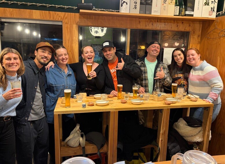 A group of people at a wooden table with drinks and snacks, in a room with wooden walls and shelves with items. 5