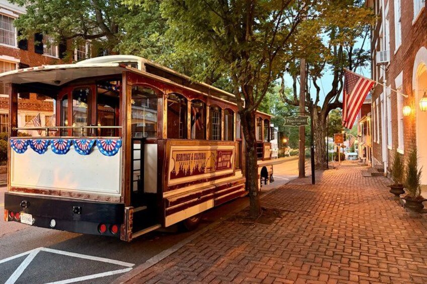 A vintage trolley on a brick street with American flags and historic buildings. 1