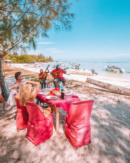 A beachside dining setup with a table, chairs, and a view of the sea and boats. 4