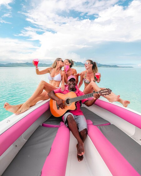 A group of people on a boat with a guitarist, surrounded by water and mountains. 1
