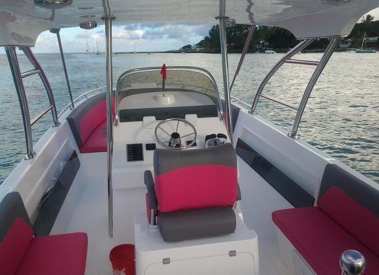 A boat's interior with a steering wheel, red and gray seats, and a view of calm water with distant land and other boats. 3