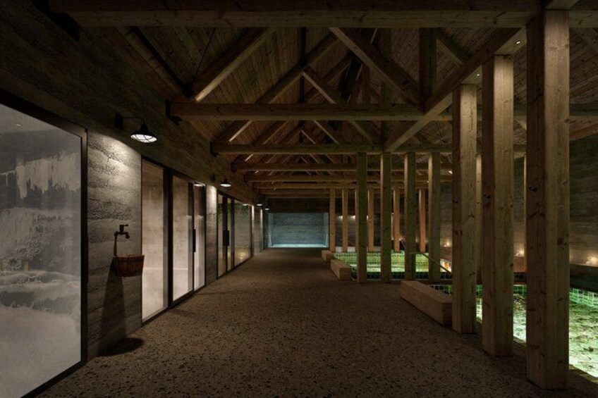 A long corridor with wooden beams, a concrete floor, and a view of a green outdoor area through large windows. 5