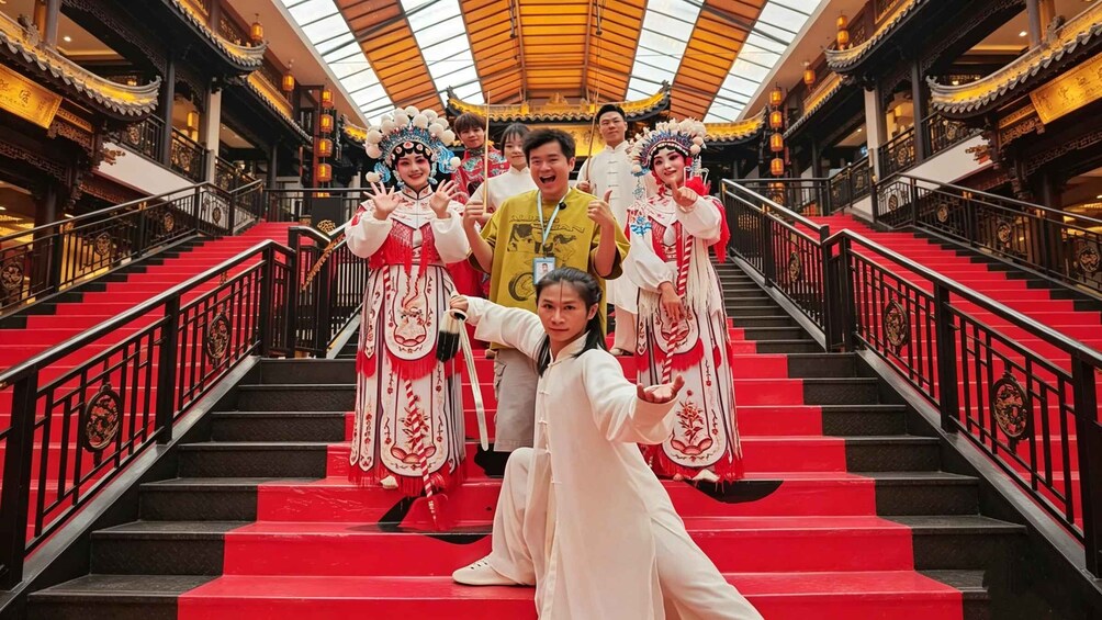 A group of people in traditional Chinese opera costumes on a grand staircase with red steps and ornate railings. 1