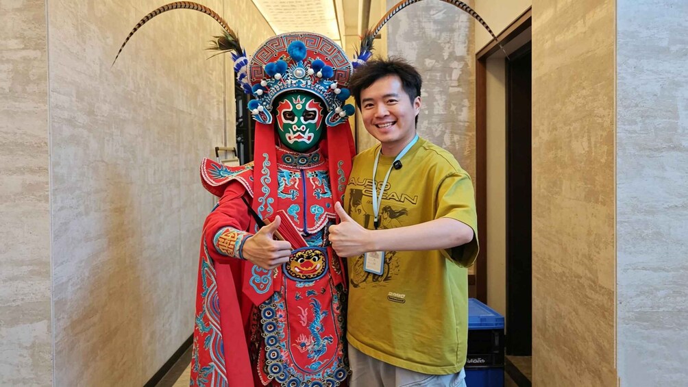 A person in traditional red and blue costume with elaborate headgear, standing in a hallway. 2