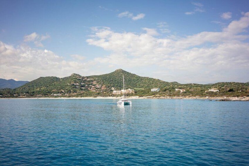A calm sea with a sailboat anchored near a coastline, surrounded by hills and buildings. 5