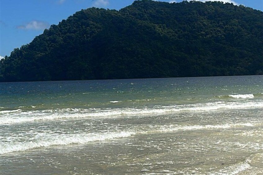 Ein Strand mit Wellen, einem sandigen Ufer und einem bewaldeten Hügel im Hintergrund. 4