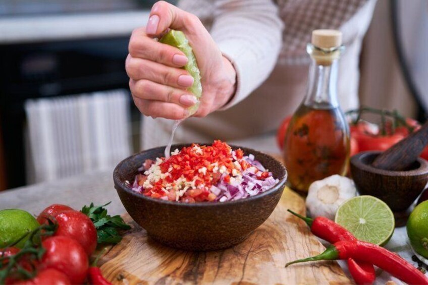 A person preparing a salad with a bowl of chopped vegetables, a lime, and a bottle of oil on a wooden table. 3