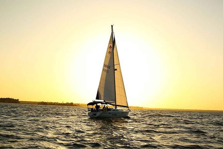 A sailboat on a body of water with a sunset in the background. 1