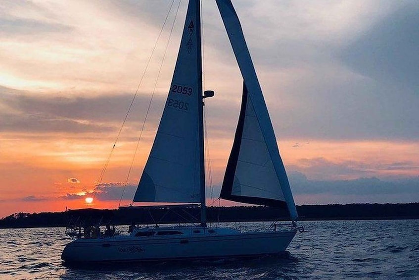 A sailboat with white sails on calm water during sunset. 4