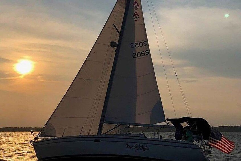 A sailboat with a number 2053 on its sail, sailing on water with a sunset in the background. 2