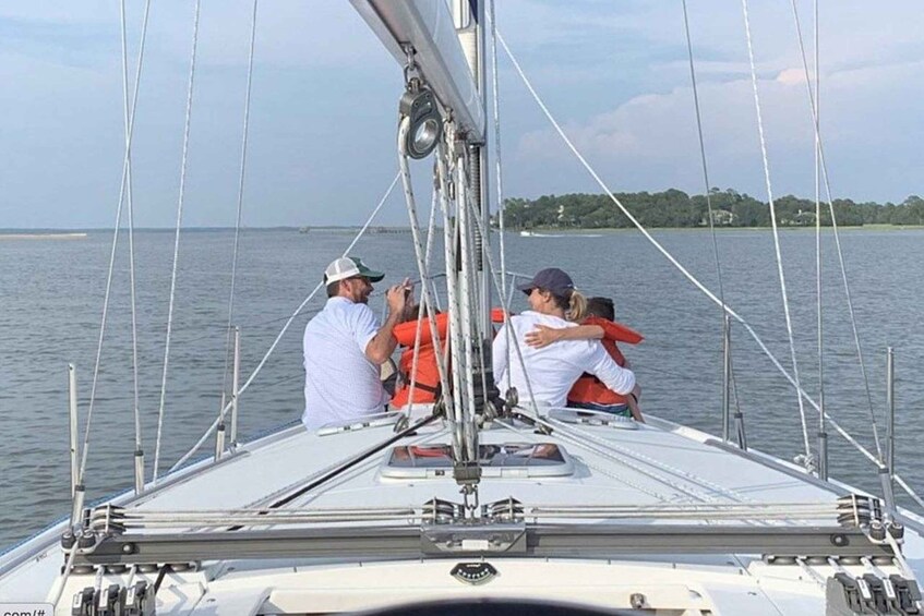A sailboat with multiple people on deck, a clear sky, and calm water. 5