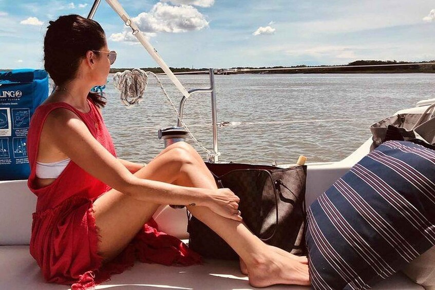 A person sitting on a boat, wearing a red dress, with a bag and a striped pillow. 4