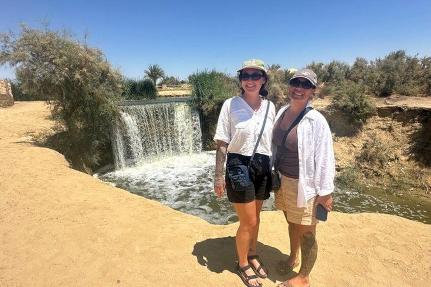 Two people standing near a waterfall in a desert landscape. 4