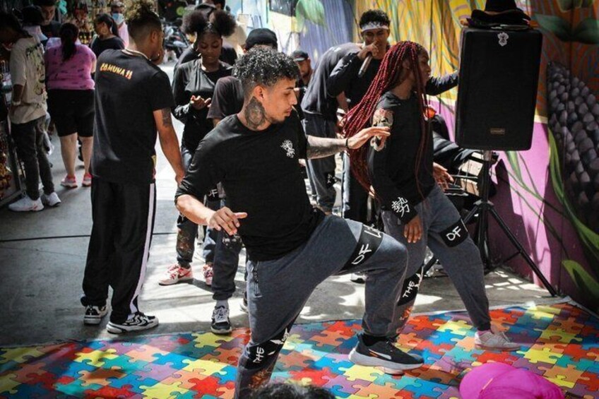 People dancing on a colorful floor with a speaker and a mural in the background. 3