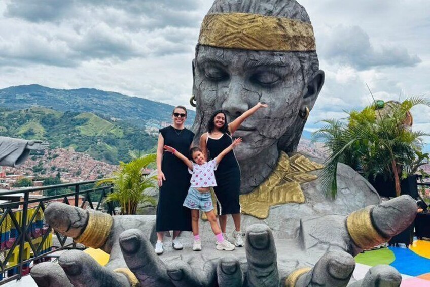 A family posing in front of a large sculpture with a mountain backdrop. 1