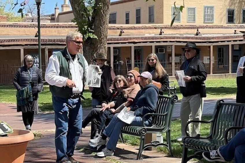 A group of people sitting on benches in a park with a building in the background. 5