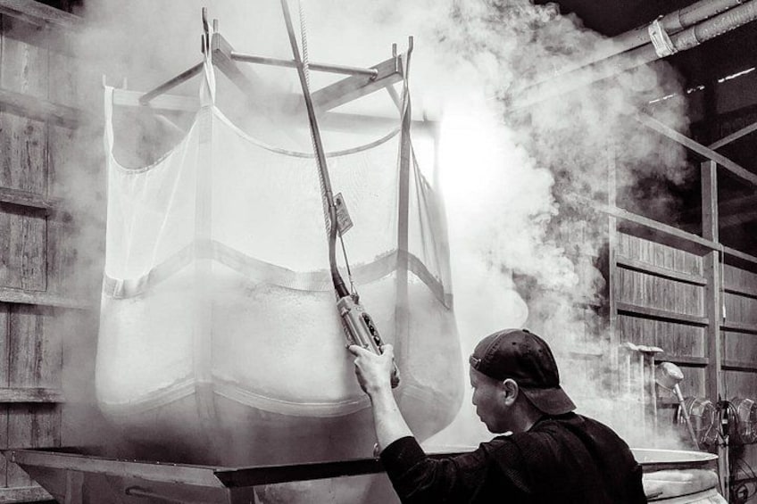 A person handling a large, transparent object with a hose, in a room with wooden shelves and a metal structure. 1
