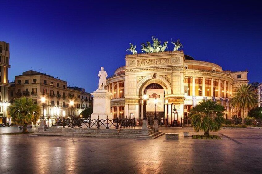 A historic building with a statue in front, surrounded by palm trees and a paved square. 1