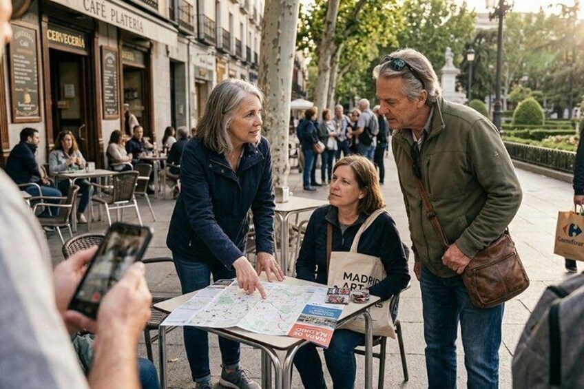 People at an outdoor cafe with tables, a map, and a sign reading 'MADRID ART.' 1