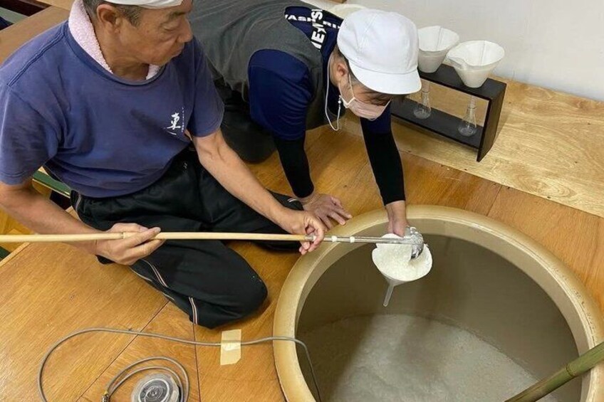 Two people working with a large wooden container, possibly a barrel, and a smaller container with a white substance inside. 3
