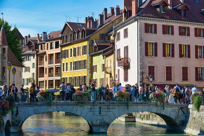 A stone bridge over a river with people walking on it, surrounded by colorful buildings. 3