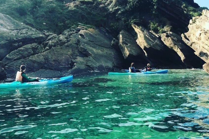 Two people kayaking on clear water with rocky cliffs in the background. 4