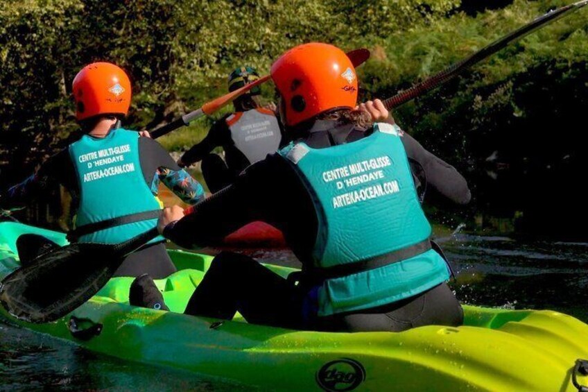 Two people in a kayak wearing life jackets and helmets, paddling on a river. 2
