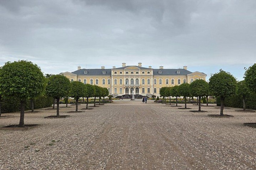 A large classical building with symmetrical architecture, surrounded by a gravel courtyard and evenly spaced trees. 2