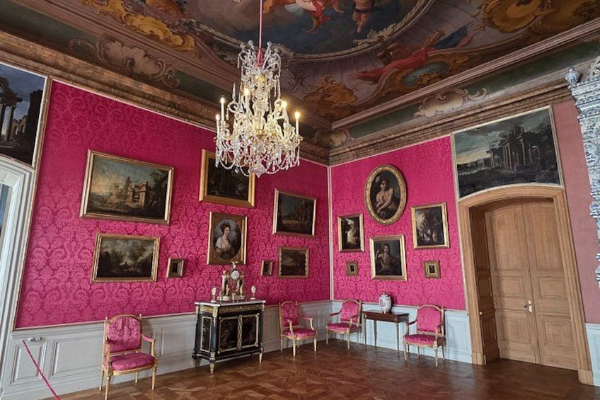 A room with pink wallpaper, wooden floor, and a chandelier. 1