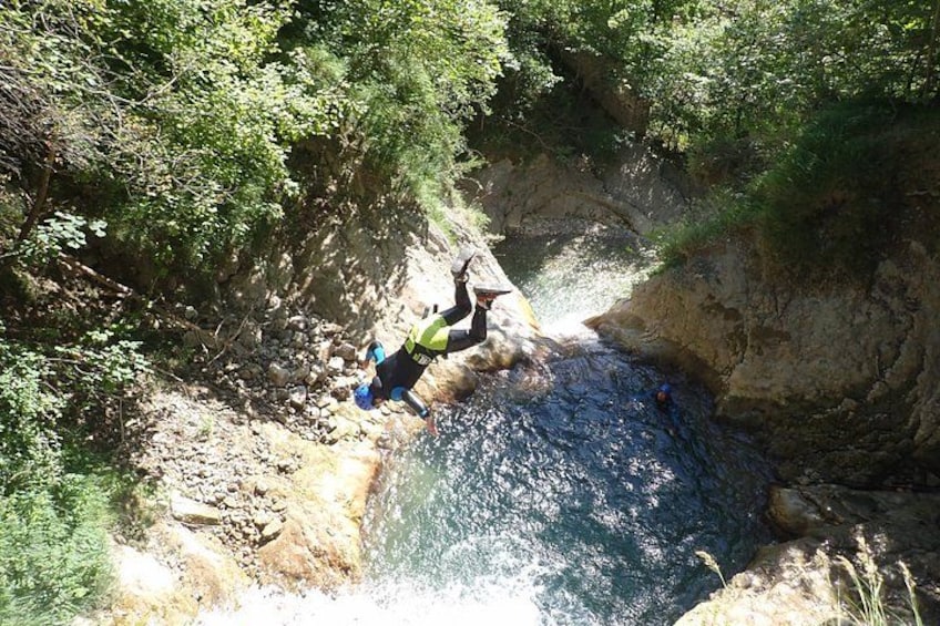 A person rappelling down a rocky cliff into a body of water surrounded by dense greenery. 5