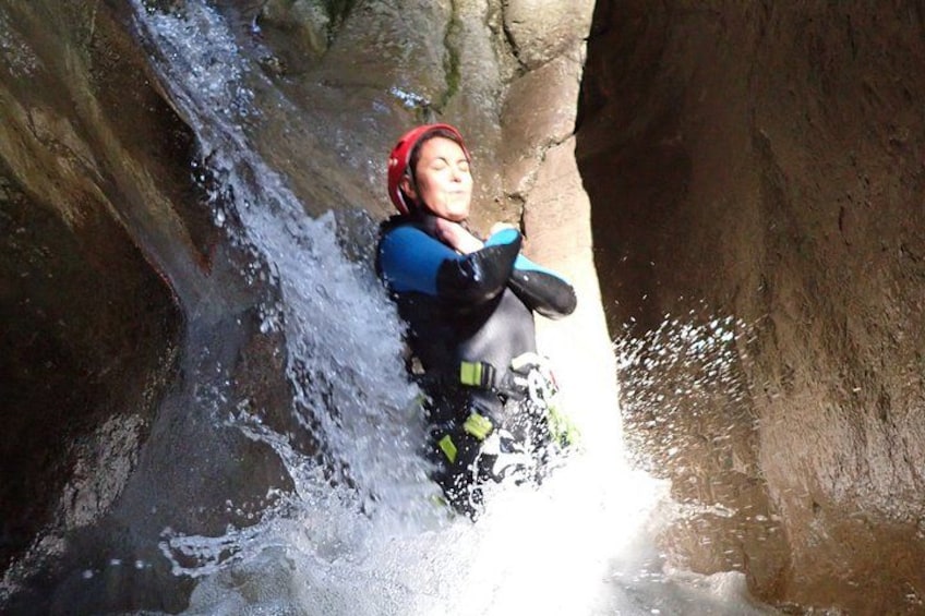 A person in a blue wetsuit and red helmet navigating a water slide in a rocky canyon. 3