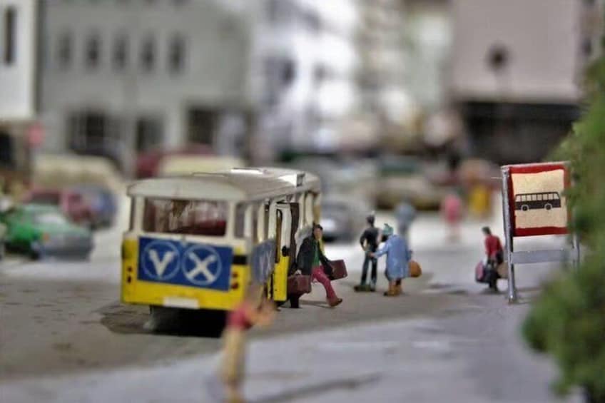 A miniature city street with a bus, pedestrians, and a bus stop sign. 5