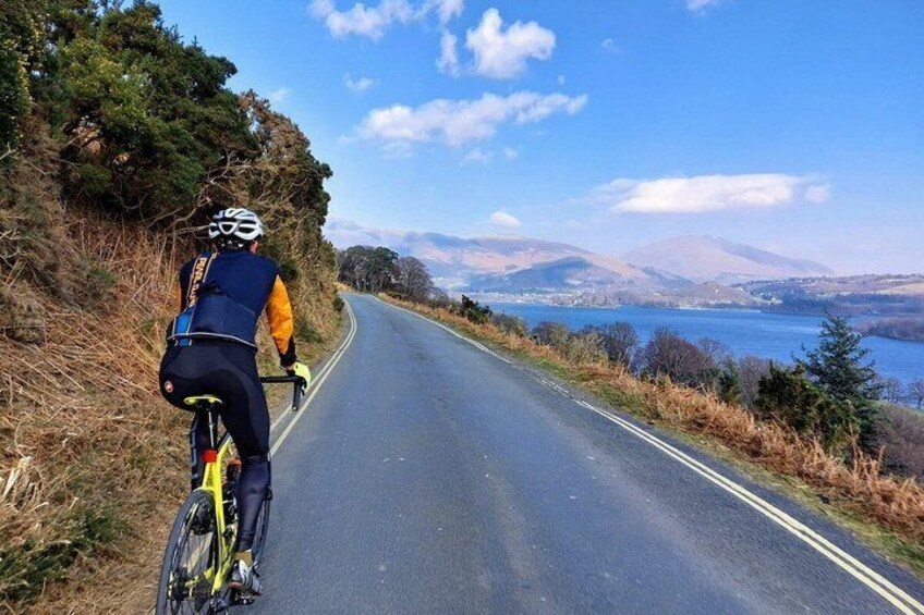 A cyclist on a road with a scenic view of mountains and a body of water. 3