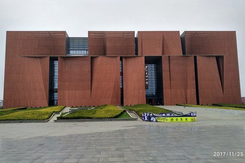 A modern building with a unique architectural design, featuring large, angular structures and a paved plaza in front. 1