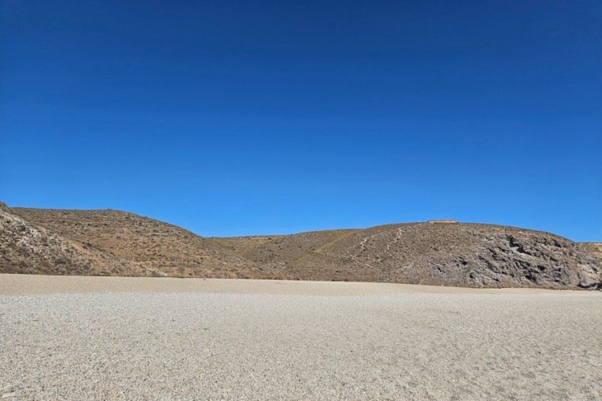A desert landscape with a clear sky, a flat sandy area, and rocky hills in the background. 4