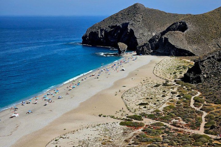 A beach with people, a clear blue sea, and rocky cliffs. 1