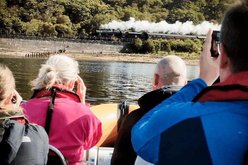 A group of people on a boat watching a train. 3