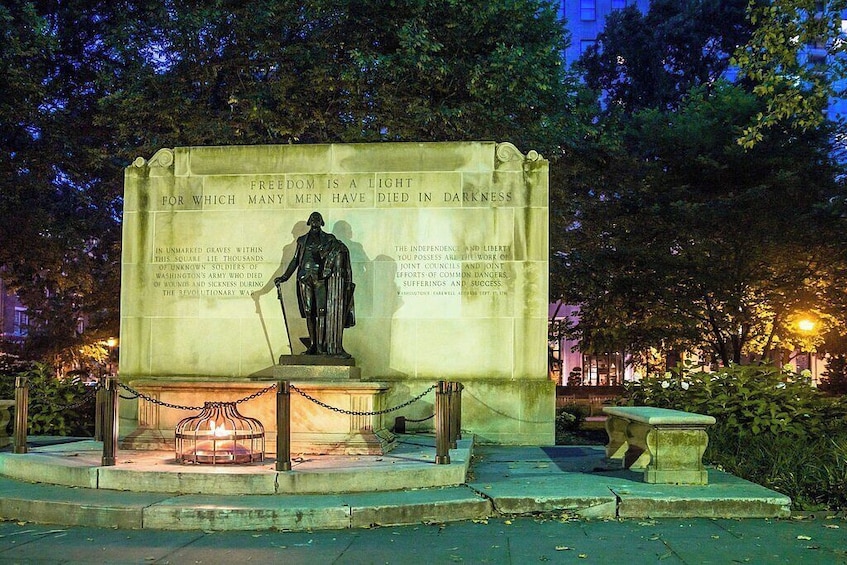 A statue of a man with a torch, surrounded by a plaque with text, in a park at night. 2
