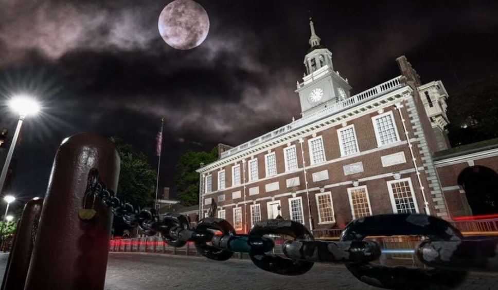 A chain-link fence, a large moon, and a historic building with a clock tower. 1