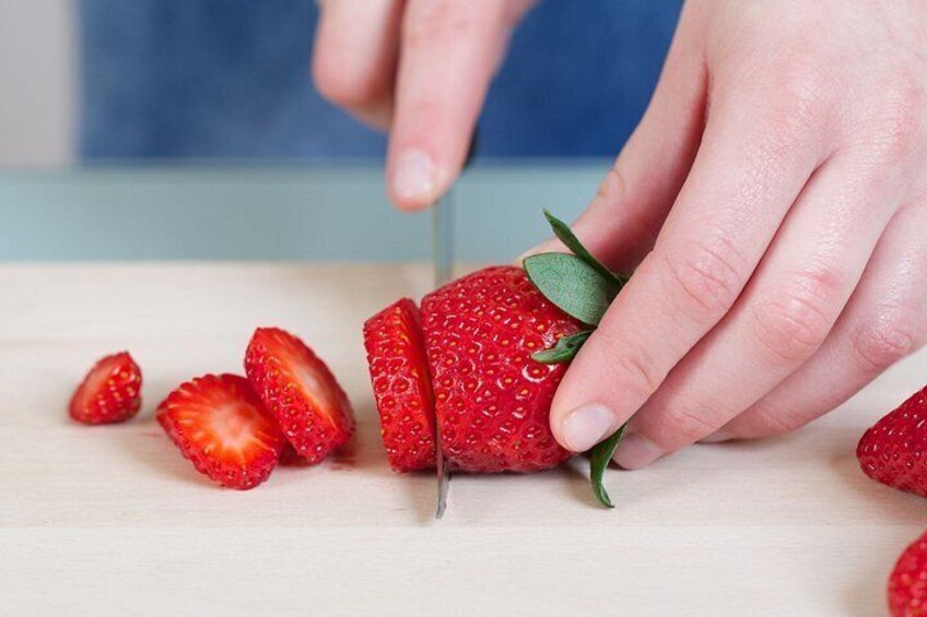 A person slicing a strawberry on a wooden surface. 3