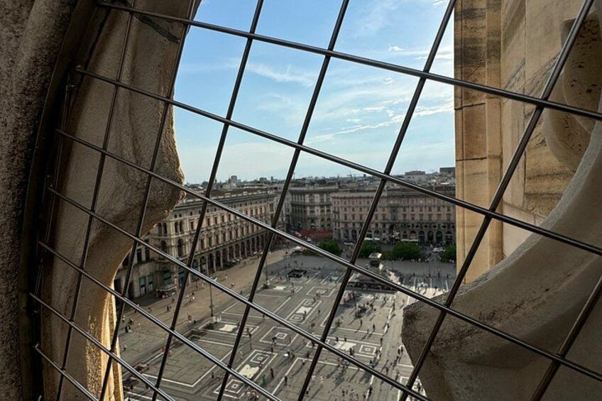 A view through a metal grid, overlooking a cityscape with historic buildings and a wide street. 5