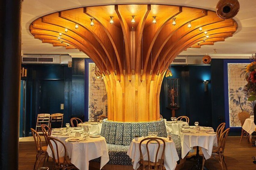A restaurant interior with round tables, a central wooden structure, and a blue patterned sofa. 4