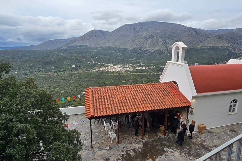 A building with a red roof, a white wall, and a bell tower. In the background, there are mountains and a valley. 1