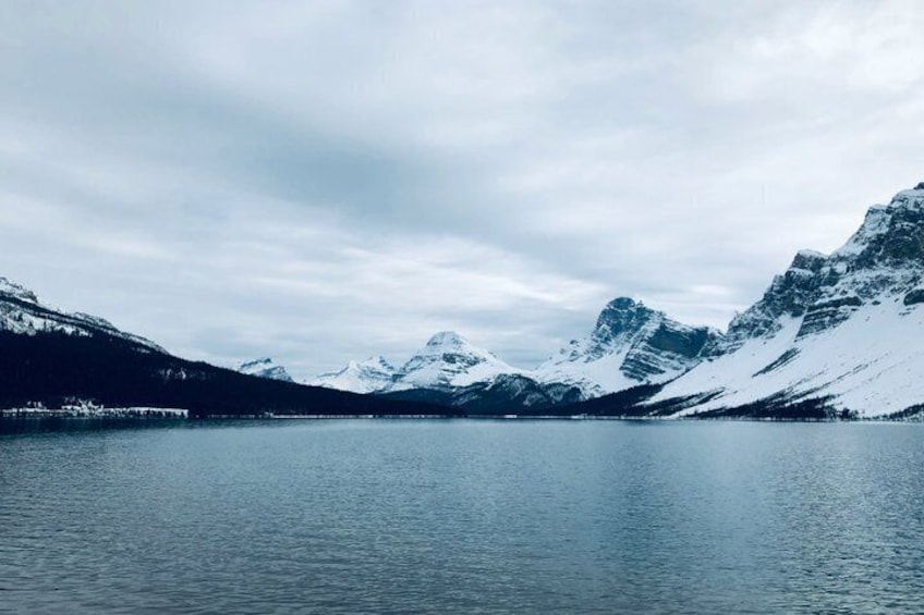 A calm lake surrounded by snow-covered mountains under a cloudy sky. 4