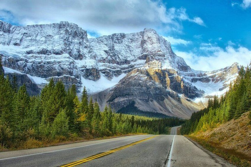A road leading through a mountainous landscape with snow-capped peaks and dense forests. 5
