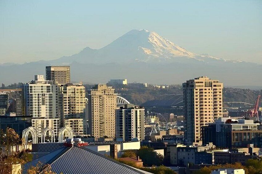 A cityscape with high-rise buildings, a bridge, and a snow-capped mountain in the background. 1