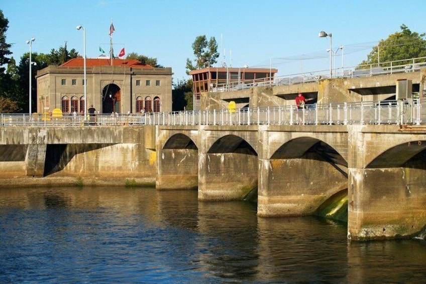 A concrete bridge with arches over a body of water, a building with a red roof, and a flagpole with flags. 4