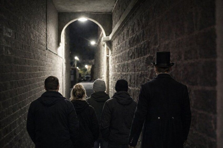 A group of people walking down a dimly lit alleyway with brick walls and a single light source at the end. 5